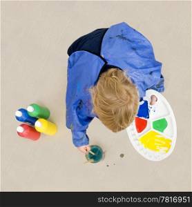 A small boy, crouching down to rinse a brush which he used with poster paint for a painting on a huge cardboard surface
