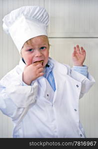 A small boy, wearing a chef&rsquo;s uniform, liking what he tastes