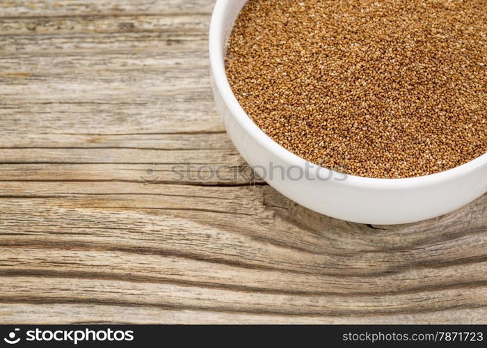 a small ceramic bowl of gluten free teff grain against weathered wood background