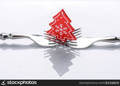 A small Christmas tree decoration on two forks on a white background. Christmas table set concept. A small Christmas tree decoration on two forks on a white background