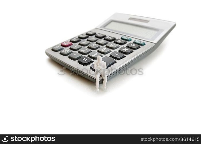 A small dummy figure sitting on a calculator over white background