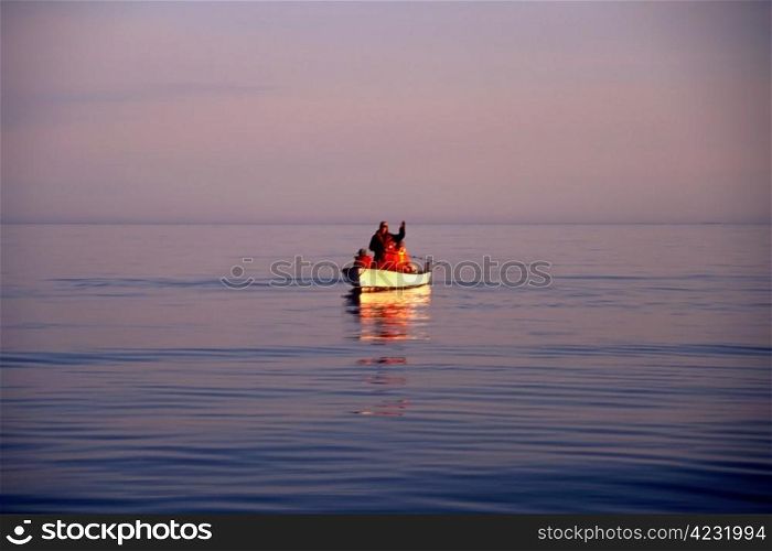 A small fishing boat with fishermen in sunset/sunrise