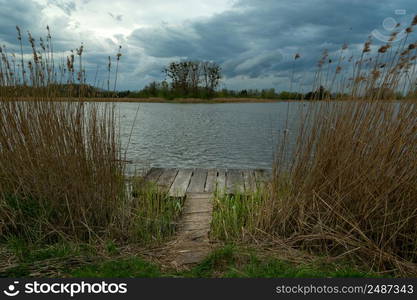 A small fishing pier in the reeds and cloudy sky, spring day