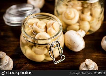 A small glass jar with pickled mushrooms on the table. On a wooden background. High quality photo. A small glass jar with pickled mushrooms on the table.