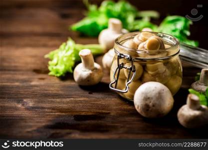 A small glass jar with pickled mushrooms on the table. On a wooden background. High quality photo. A small glass jar with pickled mushrooms on the table.