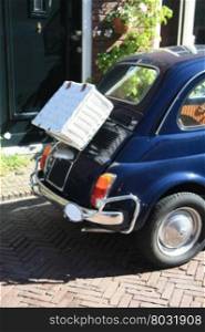 A small Italian car with a wicker suitcase on the back