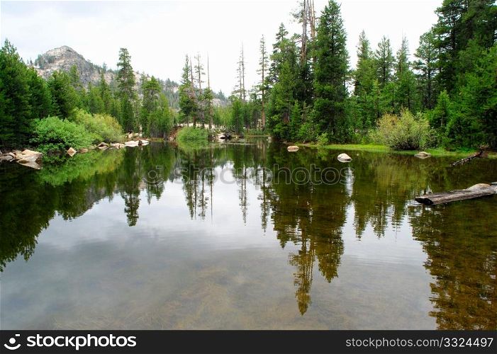 A small lake high in the california sierra nevada mountains with the surrounding forest reflected in the water.. Glassy Mountain Lake