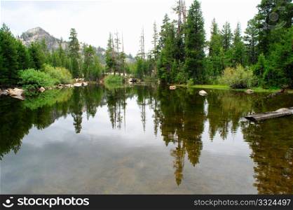 A small lake high in the california sierra nevada mountains with the surrounding forest reflected in the water.. Glassy Mountain Lake