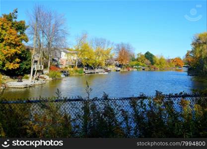 A small lake with bright colored trees under bright blue sky in the autumnwith a fence in the front.
