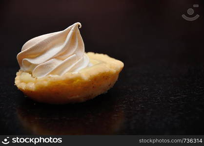 A small lemon meringue tart on a black background