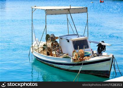 A small old wooden fishing boat with betallic reels for reeling up fishing nets, which sways in motion on the waves at the pier.. View of a small wooden fishing boat with fishing tackle.