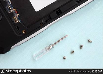 A small screwdriver and a few screws on a blue background. Tools for the repair and disassembly of modern smartphones and mobile devices. Tools for repair and disassembly of modern smartphones and mobile devices