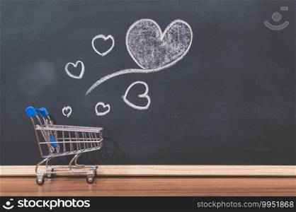 A small shopping cart and a heart shaped on a blackboard