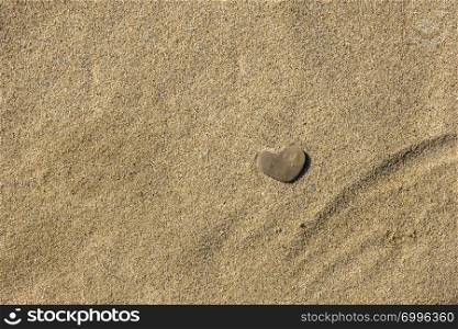 A small stone in the form of heart lies on the sand.