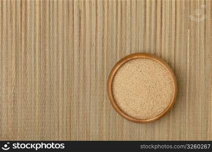 a small wooden bowl of amaranth grain on a grass mat