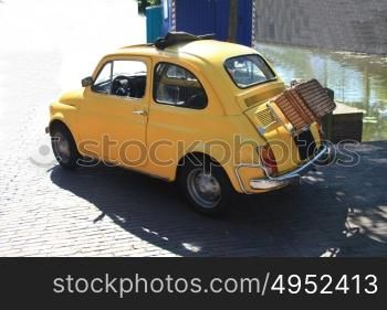 A small yellow Italian car with a wicker suitcase
