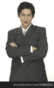 A smart asian businessman in a grey suit stands with arms folded