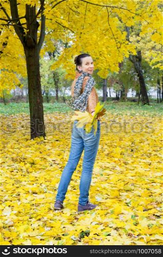 A smiling adult caucasian woman is running away with yellow maple leaves in autumn in the park