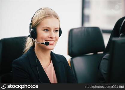 A smiling beautiful woman sitting in a customer service department office with headset working in call centre