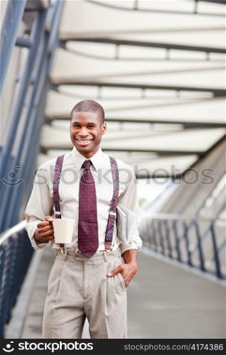 A smiling black businessman holding a coffee cup and newspaper outdoor