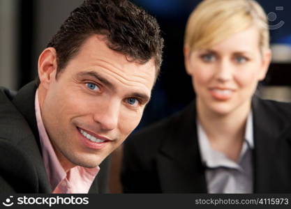 A smiling businessman and his female colleague out of focus behind him