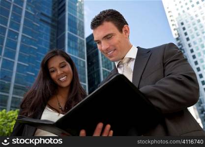 A smiling businesswoman and her male colleague taking part in a happy business meeting outside in a modern city environment