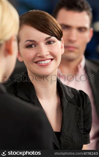 A smiling businesswoman meeting and greeting her female colleague while out of focus behind her iss her male colleague