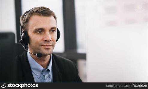 A smiling handsome man sitting in a customer service department office with headset working in call centre