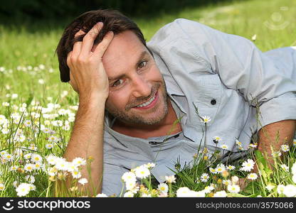 A smiling man lying in a garden amid flowers.