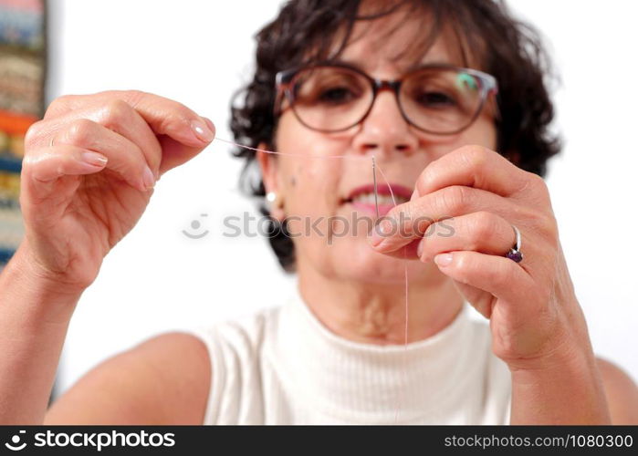 a smiling mature seamstress threading a needle