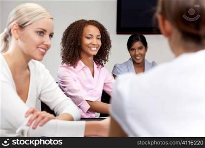 A smiling mixed race African American businesswoman and her three colleagues taking part in a happy business meeting, the focus is on the African American woman.