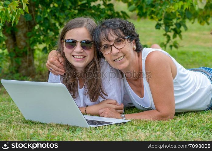 a smiling mom and daughter using a laptop at garden