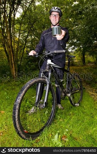A smiling mountain biker, standing next to his bike, showing a shiny steel can in his outstretched hand