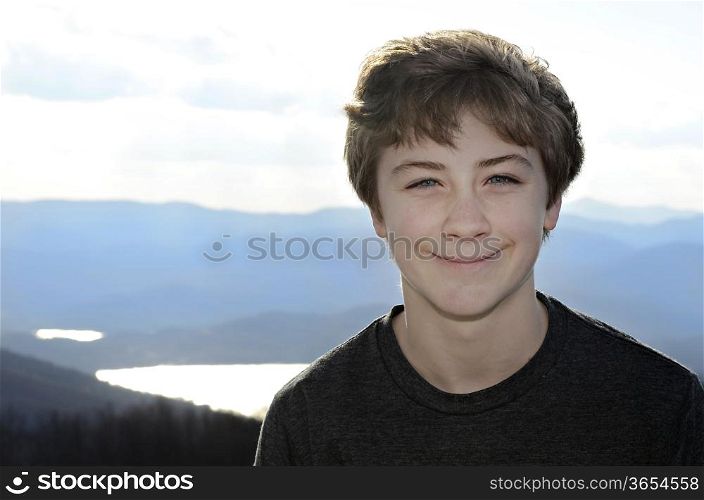 A smiling teen boy with mountains and lake in the distance.