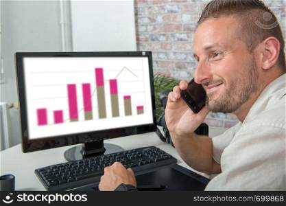 a smiling young businessman in the office talking on the phone