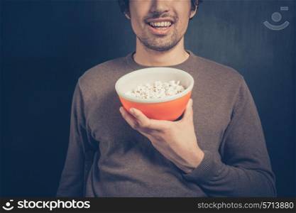A smiling young man is holding a bowl of popcorn
