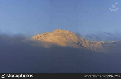 A snow-capped peak emerges from the colorful clouds of the setting sun