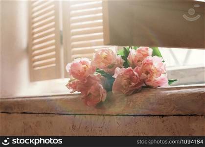 A soft focused bouquet of pink flowers lying on a window sill, wooden jalousie, gentle light in the background, rustic style. Romantic, love, care concept