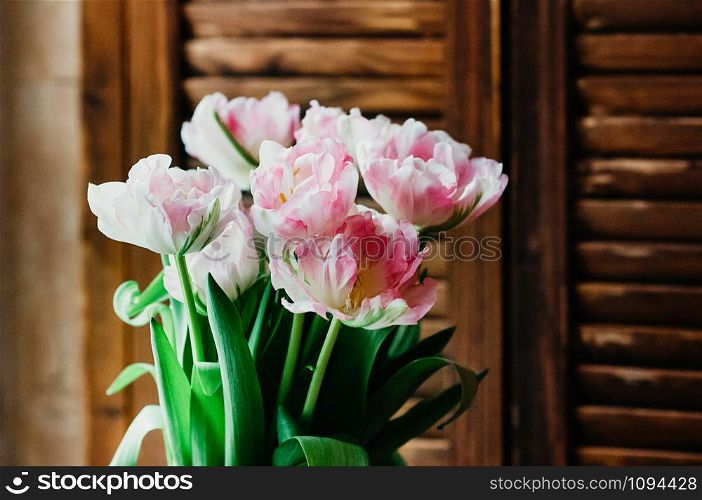 A soft focused bouquet of pink flowers, wooden jalousie in the background, rustic style, closeup view, indoors