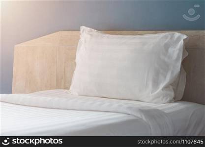 A soft pillow with white bed sheets at hotel room in the morning. Loft style hotel interior design.