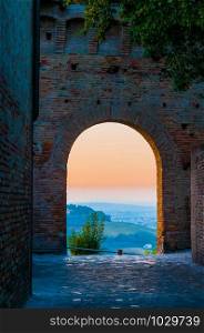 A soft sunset seen through an arch of the medieval town of Gradara in Italy