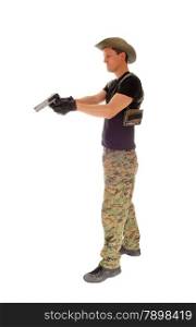 A soldier in camouflage pants, hat and black t-shirt aiming his hand gunisolated on white background.