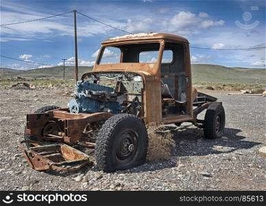 A solitary old pickup truck, abandoned in a gravel parking lot and exposed to the elements in Eastern Washington, is rusting while being scavenged for parts.