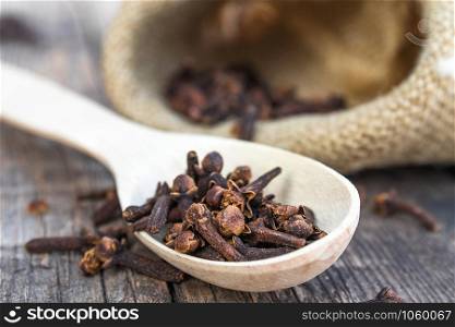 A spice of dried cloves lies on a wooden spoon and is scattered on old wooden boards near the bag. Spices cloves for cooking. Close-up.. A spice of dried cloves lies on a wooden spoon and is scattered on old wooden boards near the bag.