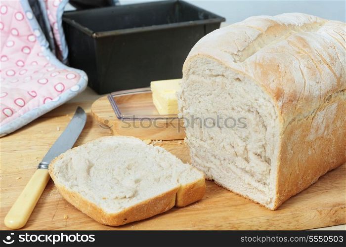 A split tin loaf of bread straight from the oven, with the crust sliced off. Butter, the baking tin and an oven glove are in the background.