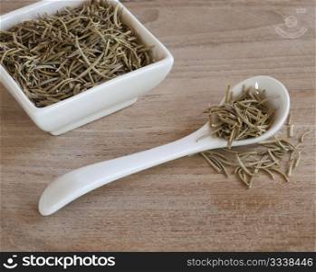 A Spoon and Dishful Of Dried Aromatic Rosemary Leaves, Up On A Wooden Work Surface
