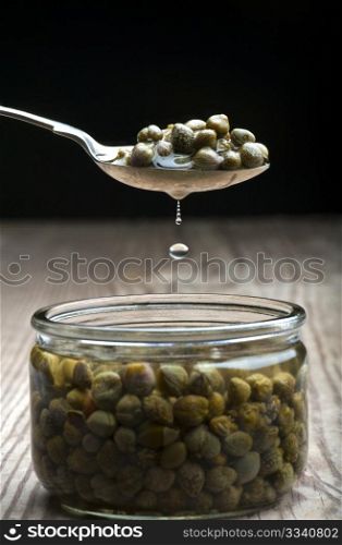 A Spoonful Of Capers Dripping Over A Jar, On A Wooden Kitchen Table
