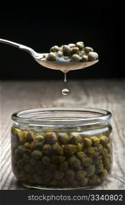 A Spoonful Of Capers Dripping Over A Jar, On A Wooden Kitchen Table