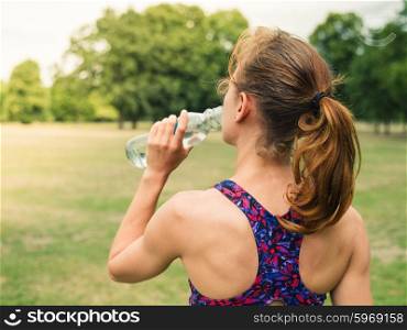 A sporty young woman is drinking water from a bottle in the park