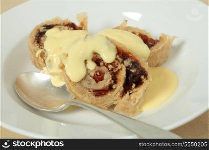 A spotted dick English pudding served with custard, horizontal.
